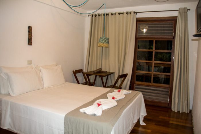 Cama de casal ainda arrumada na Pousada Taieiras em Maragogi com porta janela ao fundo