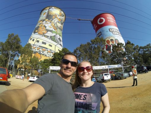 Diego e Bruna na frente das Orlando Towers que estão pintadas com cenas do cotidiano de Soweto.